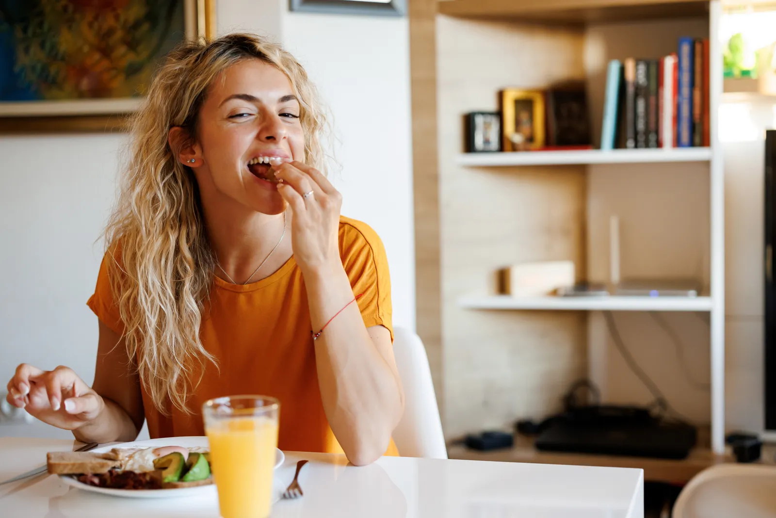 Woman grinning as she takes a bite of a snack at the table