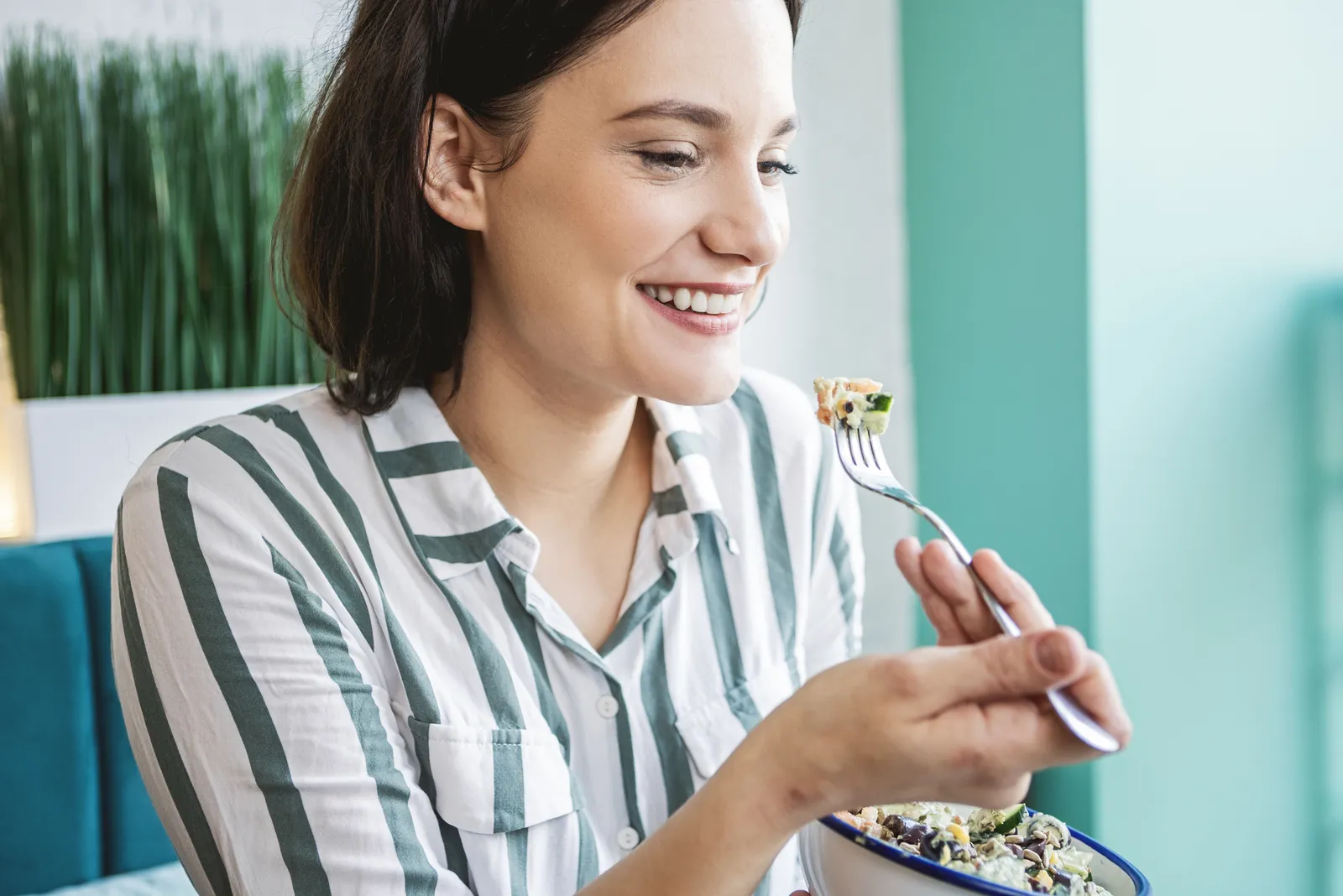 Smiling woman eating a salad bowl at home